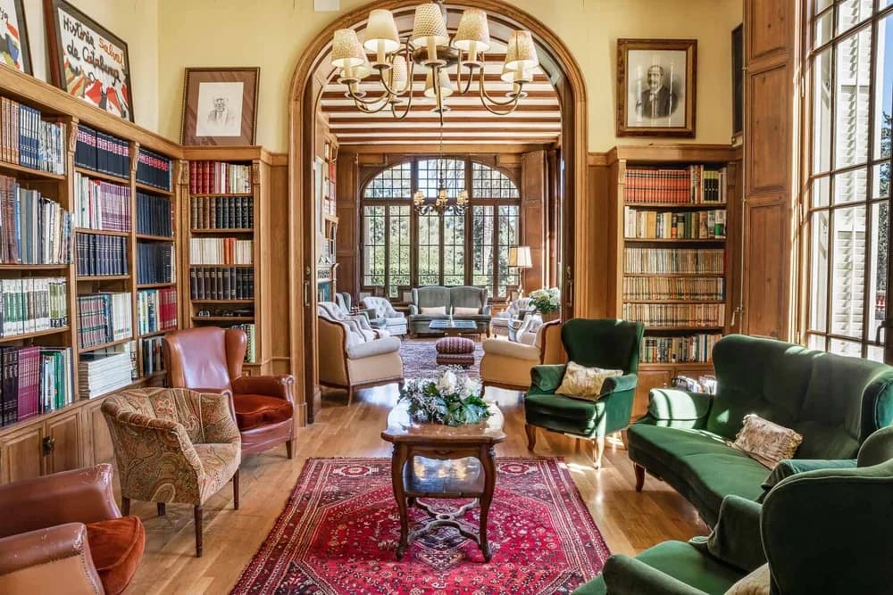 The villa's library: floor-to-ceiling wooden bookcases, worn leather armchairs and a chandelier, opening through an arch to a second sitting room