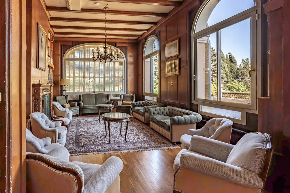 A wood-panelled salon with green velvet chesterfields, a carved fireplace and tall arched windows onto the garden
