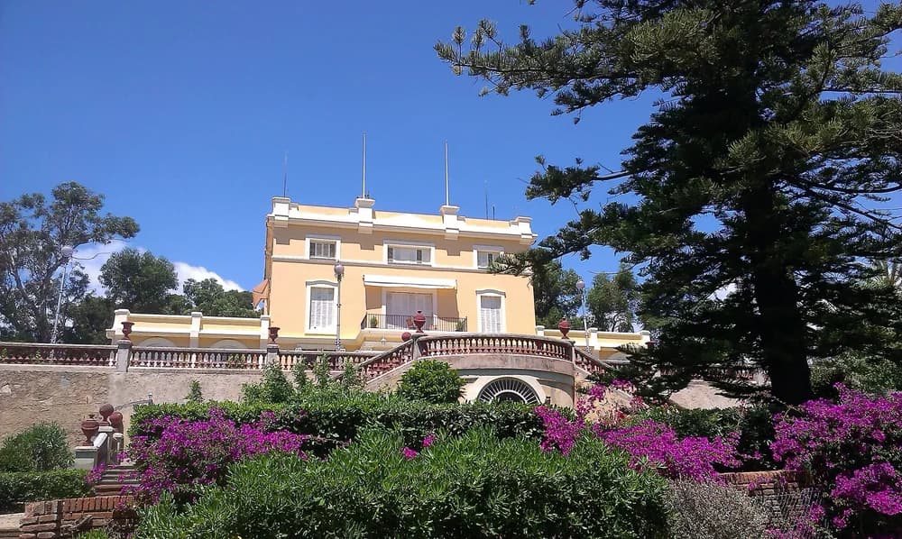 Villa Blanca seen from the garden below, its cream facade and red balustrade above flowering bougainvillea